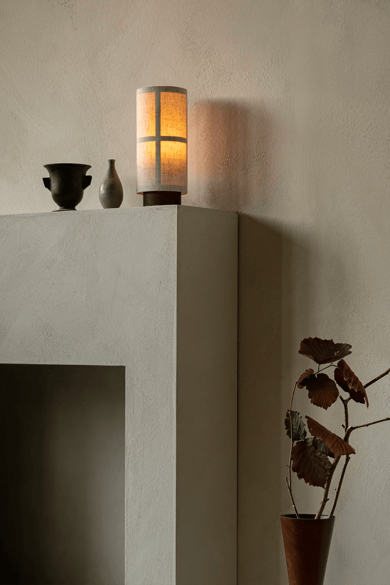Raw Hashira Portable Table Lamp by Menu, shown on a mantle, lit