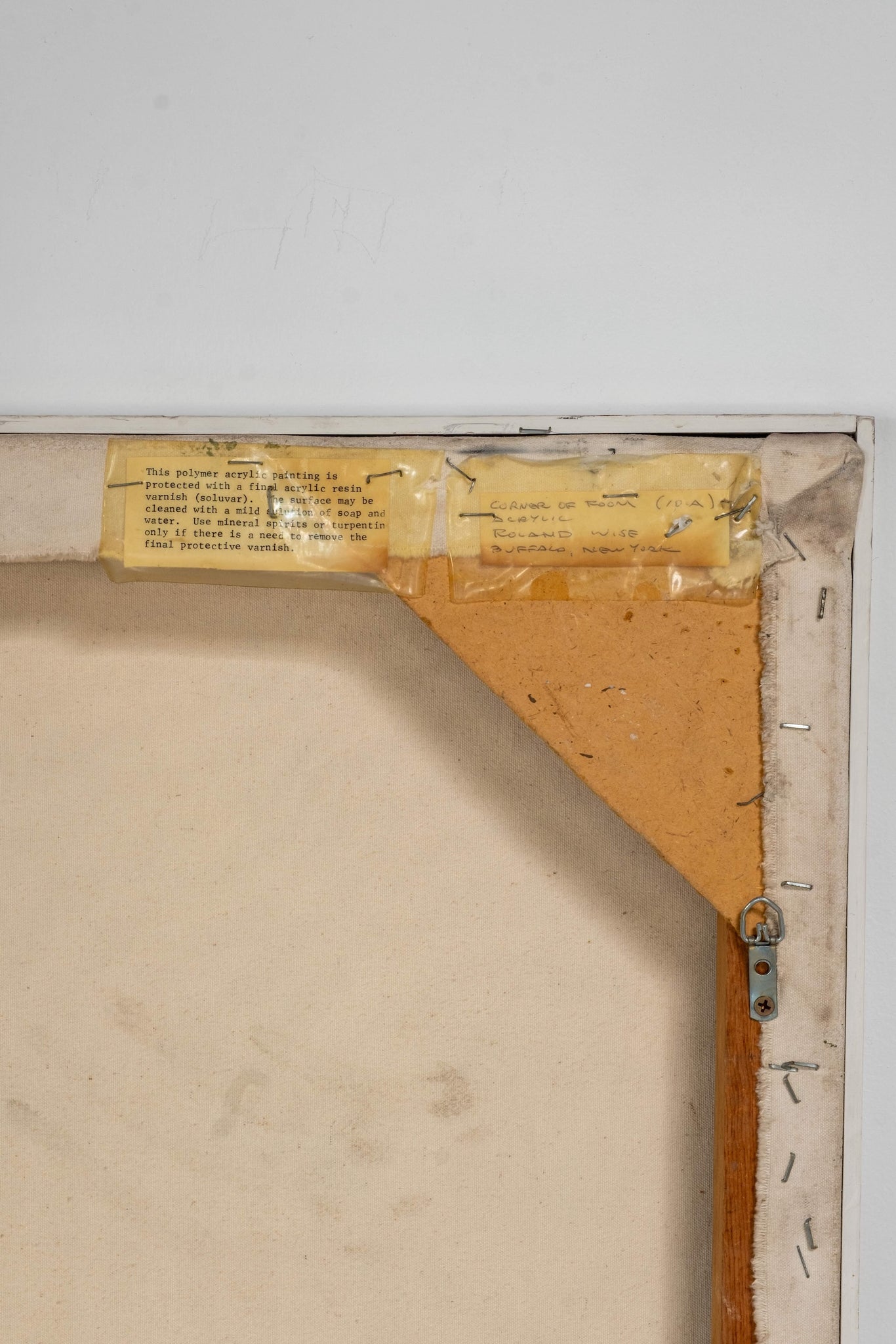 Back of a painting with a label and wooden frame corner.