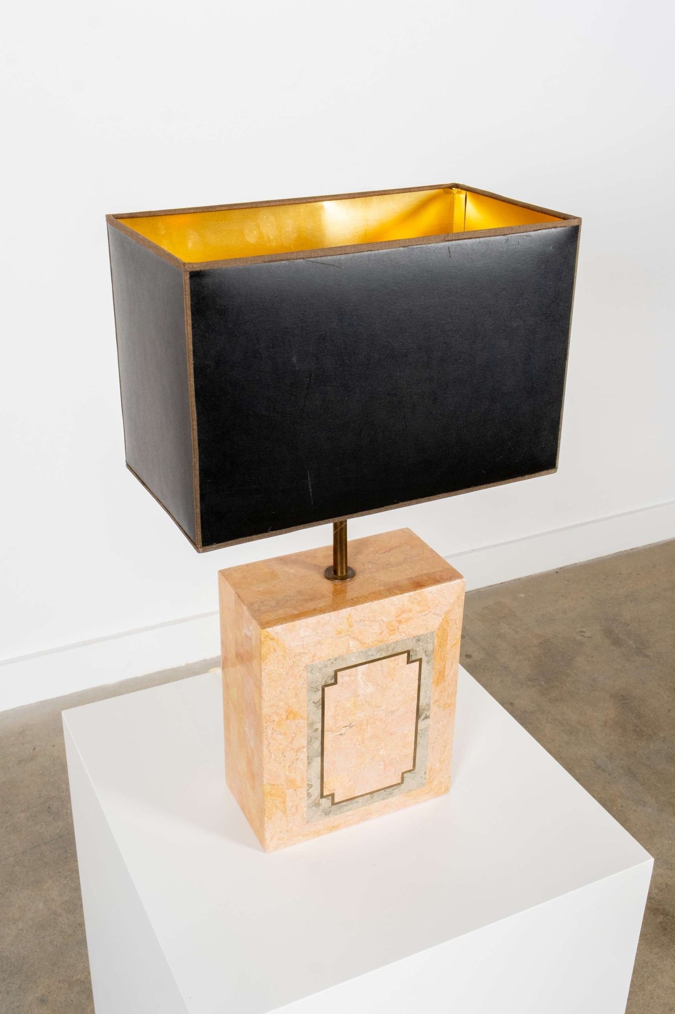 Decorative lamp with black shade and beige base on a white pedestal
