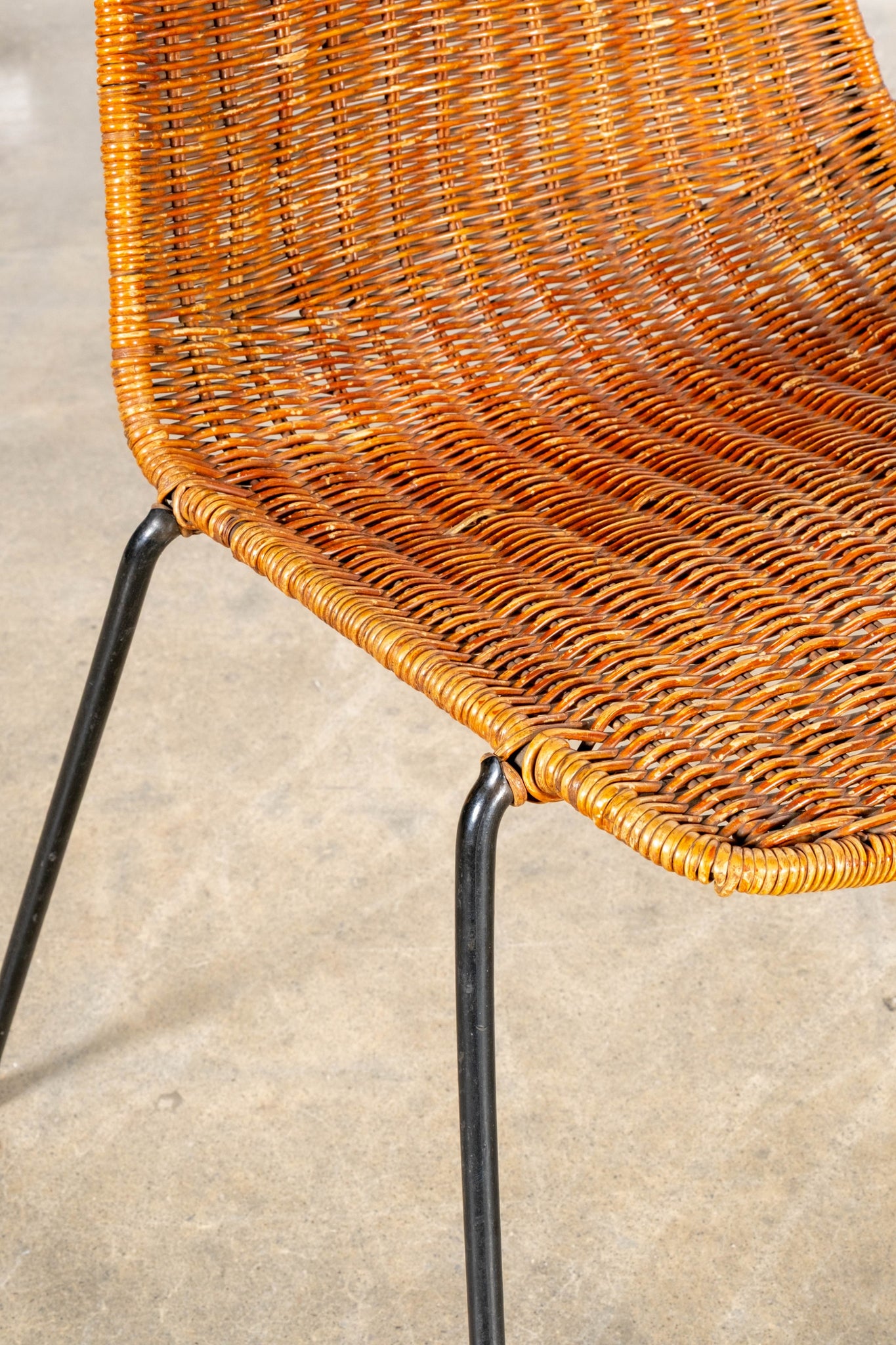Close-up of a wicker chair with black metal legs on a concrete floor.
