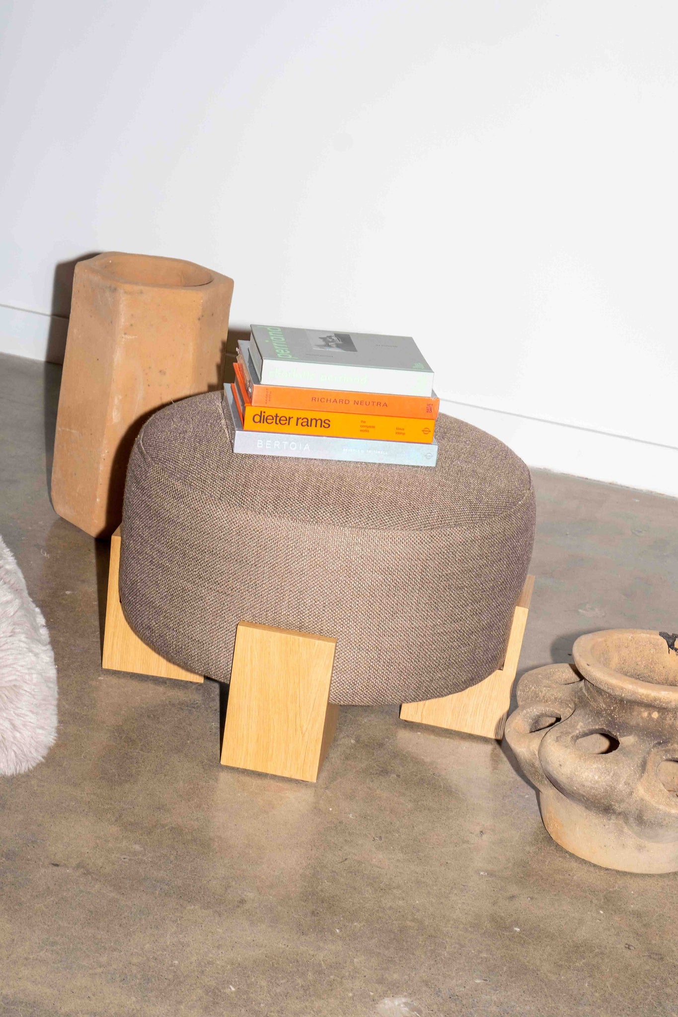 Modern ottoman with wooden legs and a textured surface, featuring books on top.